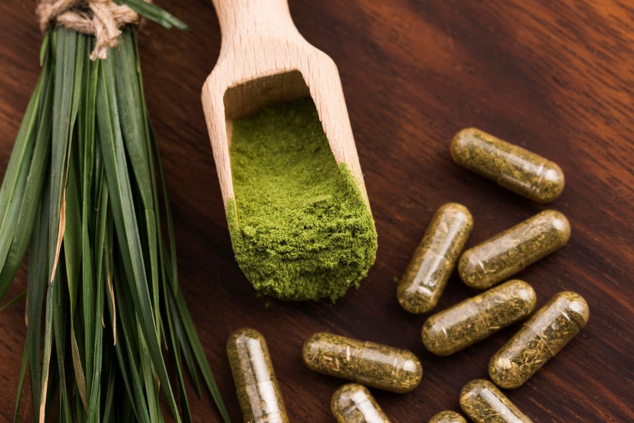 A wooden spoon with green powder on it next to some pills.
