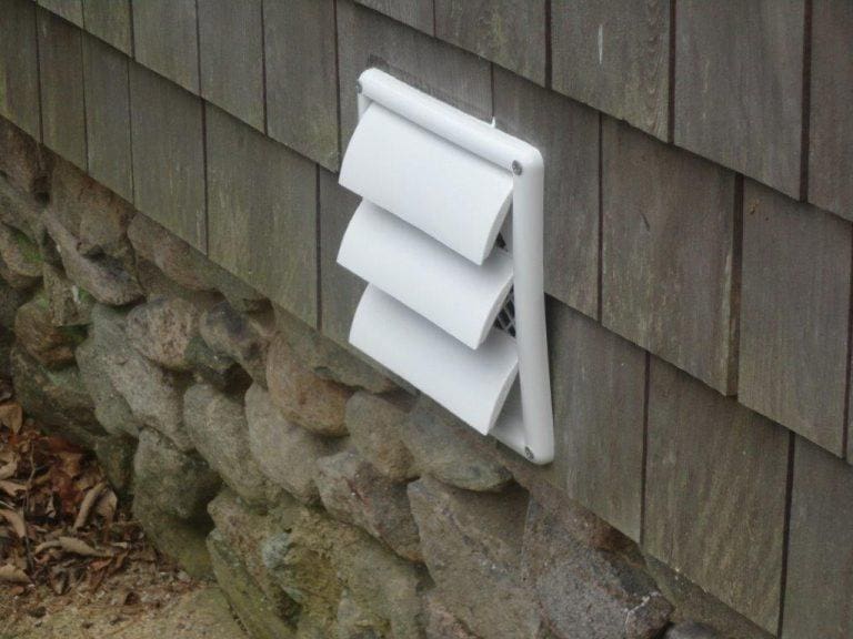 A white EZ Breathe (Taller Height), Basement Model A-400 – Standard chute – for walls up to 10′ is installed on the side of a building with wooden shingles and a stone foundation.